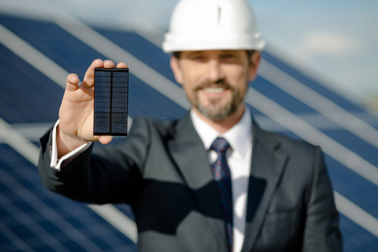 Man in business suit holding photovoltaic detail of solar panel. Businessman showing detail from solar panel.