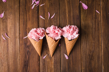Flowers in a waffle cone. Pink carnations. Flowers on a wooden  background. Copyspace. Flower photo concept