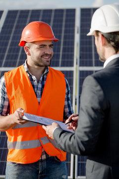 Business client signing contract for installation of solar power panels. Worker in orange helmet and vest holding folder with documents for clients signature.