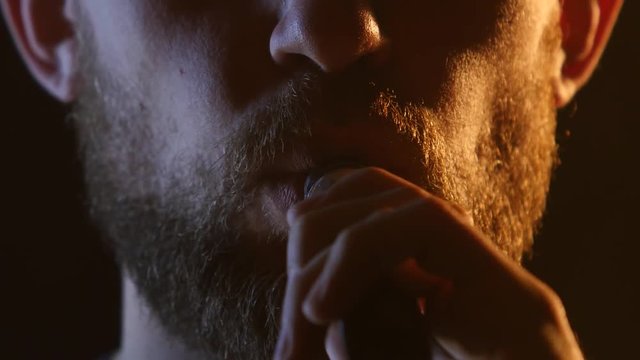 Man exhales smoke into a dark room. Black background. Close up