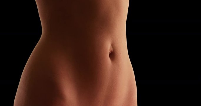 Close up of young Caucasian woman's flat stomach on black background. Closeup of white female's fit abdomen and tan skin. 4k 