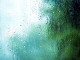 Rain drops and water stains on glass window in rainy summer day. Blue and green background