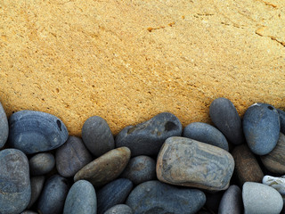 Fototapeta na wymiar Small round dark stones against the background of a large light stone. Black pebbles and a yellow boulder