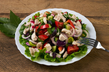 Summer fresh salad made of tomato, ruccola, chicken breast, arugula, crackers and spices and other different vegetables on wooden background