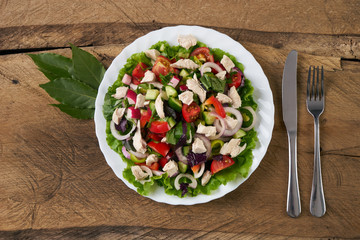 Top view of a fresh salad with smoked chicken meat and fresh vegetables: cucumber, bell pepper, garlic, onion and cherry tomatoes on old wooden table. Delicious dinner table. Healthy eating.