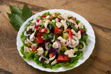 Healthy salad plate with bell pepper, tomatoes, chicken, cucumder, onion and mixed greens, lettuce, parsley on wooden background. Food and health.