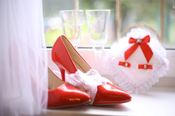 wedding bridal red patent leather high heeled shoes with rings and wine glasses still life on windowsill