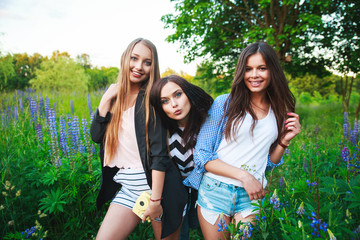 Three hipsters girls blonde and brunette taking self portrait on polaroid camera and smiling outdoor. Girls having fun together in park.