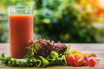 A glass of vegetable juice on wooden table with blurred natural green background