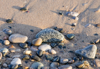 Closeup of smooth, patterned and colorful wet stones on a sandy beach