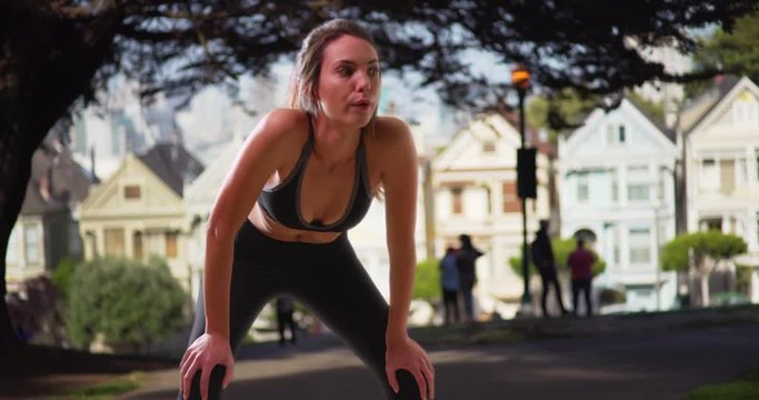Young Caucasian woman doing breathing exercises after jog in San Francisco neighborhood. Athletic millennial concentrating on breath after run in painted ladies neighborhood. 4k 