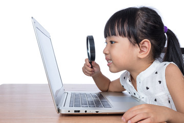 Asian Chinese little girl looking at laptop through magnifier