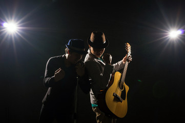 Obraz premium Musician Duo band hand holding the microphone and singing a song and playing the guitar on black background with spot light and lens flare, musical concept