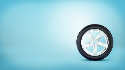 Obraz na płótnie Canvas A car wheel with five spokes standing on the tire rim on blue background.