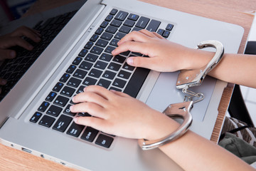 Child's hands in handcuffs with laptop