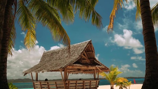 Wooden pavilion on white sand beach under palm trees with some people, Daku Island, Siargao, Philippines
