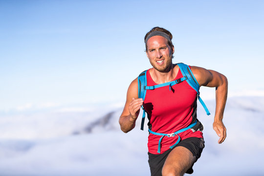 Runner trail running fitness man on endurance run - motivation and concentration on race in sky and clouds background on nature landscape. Focused athlete with backpack and hairband training cardio.