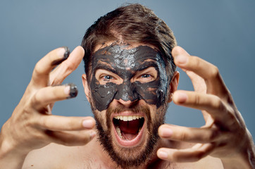 A young guy with a beard on a gray background in a clay facial mask