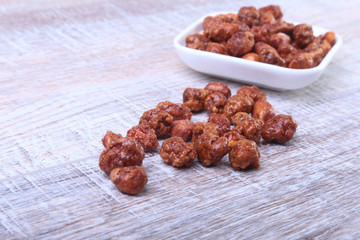 Sugared Hazelnuts in a white bowl on a wooden background. Hazelnuts in sugar glaze. Selective focus.