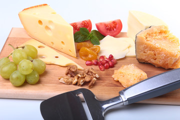 Assortment of cheese with fruits, grapes, nuts and cheese knife on a wooden serving tray.