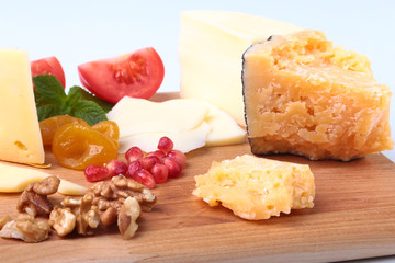 Assortment of cheese with fruits, grapes, nuts and cheese knife on a wooden serving tray.