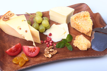 Assortment of cheese with fruits, grapes, nuts and cheese knife on a wooden serving tray.