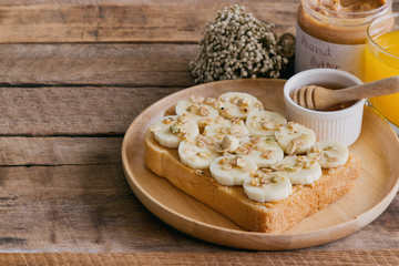 Banana peanut butter toast sandwich on wood plate with honey. Homemade open sandwich spread with peanut butter on top with banana slice and granola. Delicious healthy sandwich for breakfast or lunch.