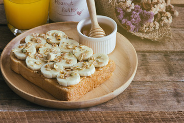 Banana peanut butter toast sandwich on wood plate with honey. Homemade open sandwich spread with peanut butter on top with banana slice and granola. Delicious healthy sandwich for breakfast or lunch.