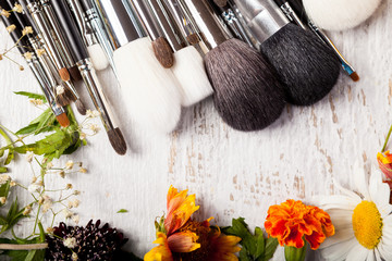 Cosmetic Make up brushes next to wild flowers on wooden background