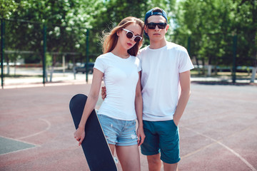 Young skater boy and girl with skateboard in white T-shirts on the basketball court. © kanashkin