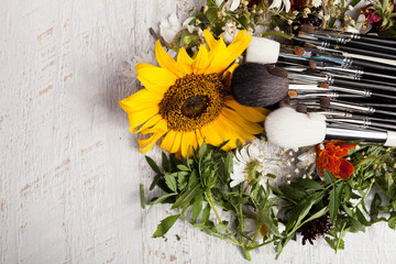 Make up brushes on a pile of wild flowers on wooden background