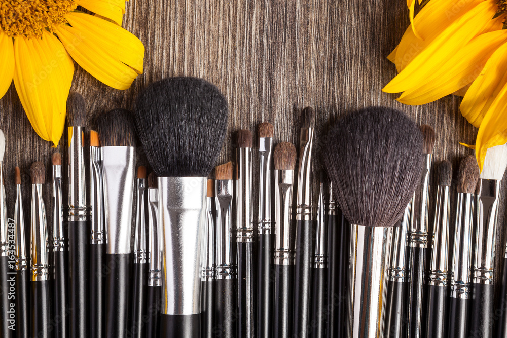 Poster professional make up brushes next to beautiful wild flowers on wooden background