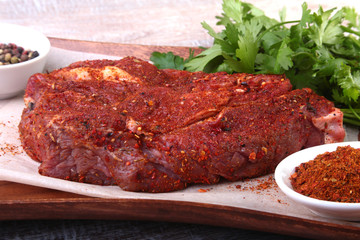 Raw beef steak with spices Leaves of coriander on wooden cutting board. Ready for cooking.