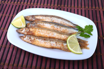 Deep frying small fish capelin and sliced lemon on white plate. Good snack to beer.