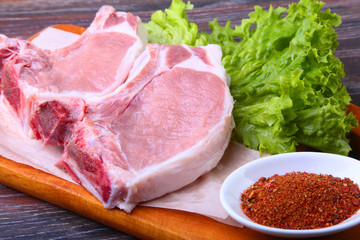 Raw pork steak with spices Leaves lettuce on wooden cutting board. Ready for cooking.