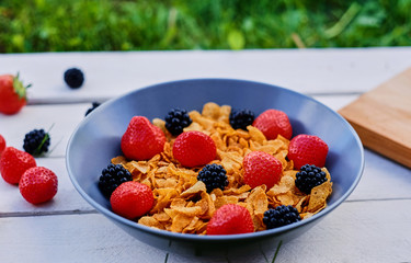 Corn flakes on a strawberry and blackberry on a plate.