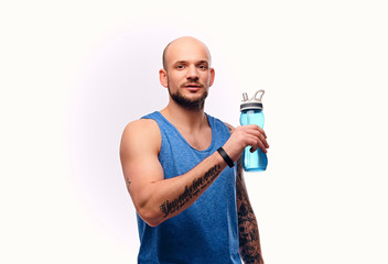 Shaved head sporty male drinks water.