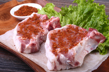 Raw pork steak with spices Leaves lettuce on wooden cutting board. Ready for cooking.
