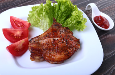 grilled pork chops with tomato, leaves lettuce and ketchup on plate.