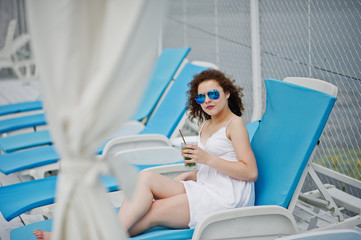 Portrait of an amazing young girl wearing sunglasses enjoying her cocktail sitting on a lounger in lakeside.