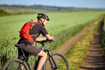 Young man riding on a bicycle on green meadow with a backpack