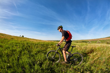 Young man riding on a bicycle on green meadow with a backpack