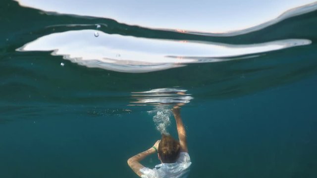 man sinking into the sea, half underwater close up, raw, 4k