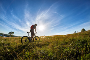 Young cyclist riding mountain bicyclist against beautiful sunset in the countryside.