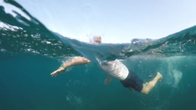 young man in a white shirt is swimming on the sea, half underwater close up, raw, 4k