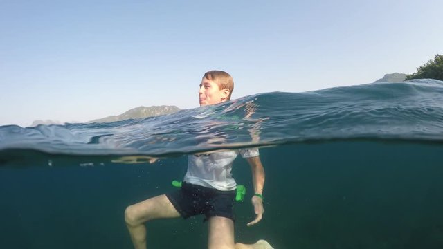 young man in a white shirt is swimming on the sea, half underwater close up, raw, 4k