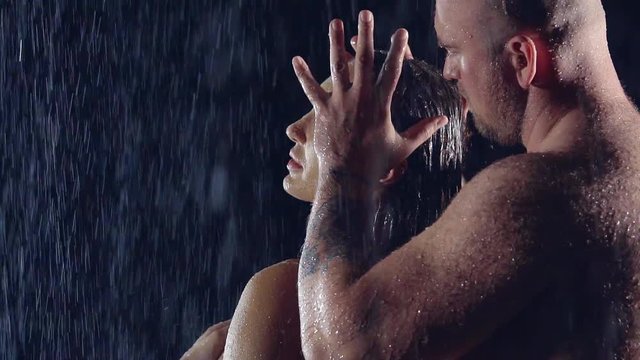bald naked man with a hairy back is with the woman in a dark room under the jets of water. he touches the girl's head, she gets great pleasure from touch.