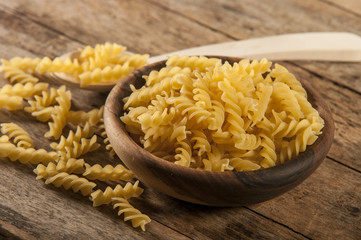 Pasta fusilli in a wooden bowl on wood background for healthy recipes.