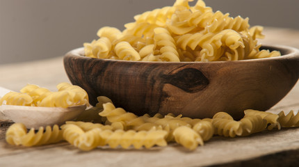 Pasta fusilli in a wooden bowl on wood background for healthy recipes.
