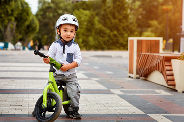 Little boy kid in helmet ride a bike in city park. Cheerful child outdoor.